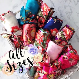 May include: A white wicker basket filled with colorful satin robes with floral patterns. The robes are tied with matching sashes. The text "all sizes" is written on a white label with watercolor flowers.