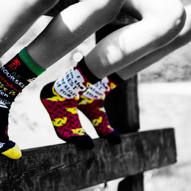 May include: A pair of colorful socks with fun sayings. One sock says "Be Yourself, Everyone Else is Taken" and the other says "I'm the Best Version of Me."