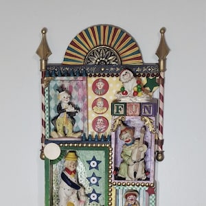May include: A colorful wooden wall art piece featuring a circus theme. It has multiple compartments with figurines of clowns, a dog, and a star. The compartments are decorated with stars, stripes, and polka dots. The top of the piece has a red, yellow, and green striped arch. The word "FUN" is spelled out in colorful blocks.