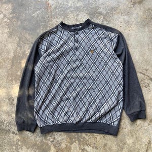 May include: A gray and black argyle patterned sweatshirt with long sleeves. The top portion features a diamond pattern with a button-up neckline and a small yellow logo. The sleeves and bottom hem are solid gray.