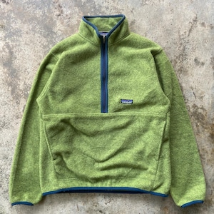 May include: A lime green fleece pullover with a quarter-length zipper closure. The garment features a high collar, long sleeves, and a large front pocket. A small Patagonia brand label is stitched on the chest. The edges are trimmed in dark blue.
