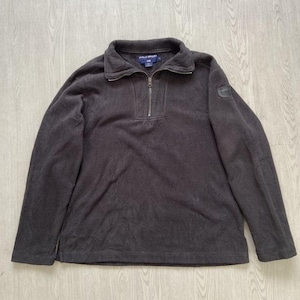 May include: A dark brown fleece pullover with a quarter-zip closure and a collared neckline. The long-sleeved top features a small logo patch on the upper left sleeve. The garment is made of a soft, textured material.