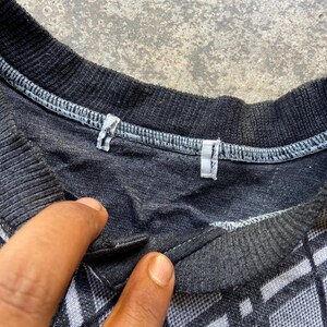 May include: Close-up of a dark gray and white patterned shirt. The shirt has a diamond pattern and a buttoned collar. The collar and neckline are dark gray.