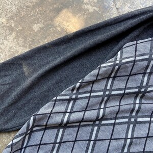 May include: A long-sleeved shirt with a gray argyle pattern on the front and a solid gray sleeve. The argyle pattern is composed of black and white lines forming diamond shapes. The shirt is made of a soft, possibly knit, material.