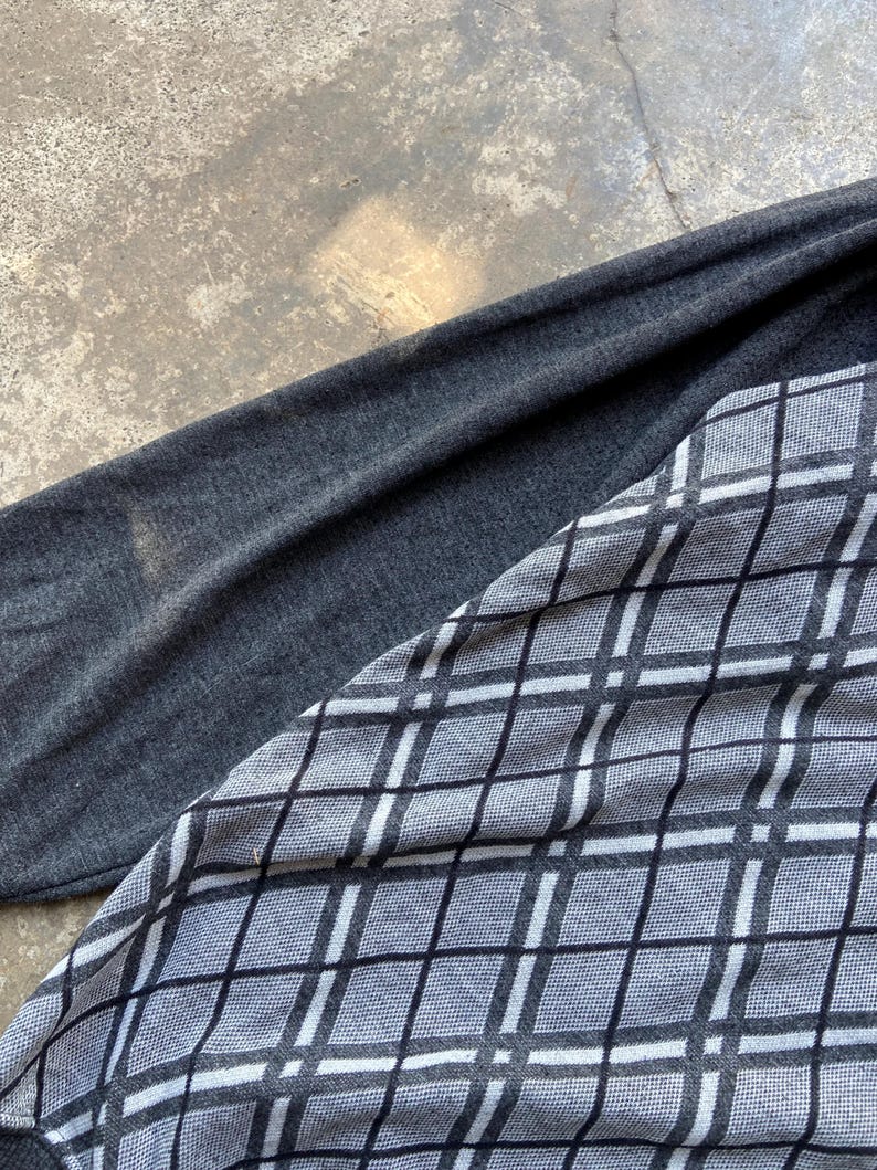 May include: A long-sleeved shirt with a gray argyle pattern on the front and a solid gray sleeve. The argyle pattern is composed of black and white lines forming diamond shapes. The shirt is made of a soft, possibly knit, material.
