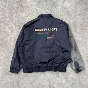 May include: Black Ferrari Sport jacket with a grey sleeve. The jacket features the Ferrari logo and the text "FERRARI SPORT" and "MAGNETI MARELLI" in white and green. The jacket has a ribbed hem and collar.