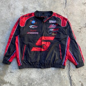 May include: A black and red racing jacket featuring the Snap-on logo on the chest and shoulders. The jacket includes various embroidered sponsor logos such as Ganassi Racing, Doug Herbert, and Pedregon Racing, with a stand-up collar and long sleeves.