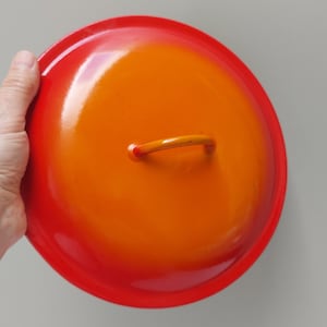May include: Orange and red enamel cast iron pot lid with a yellow handle.