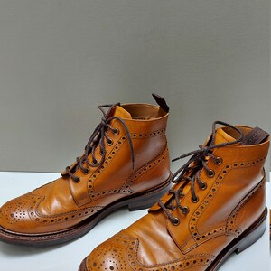 May include: A pair of brown leather brogue boots with a lace-up closure. The boots have a wingtip design and a decorative pattern of small holes.