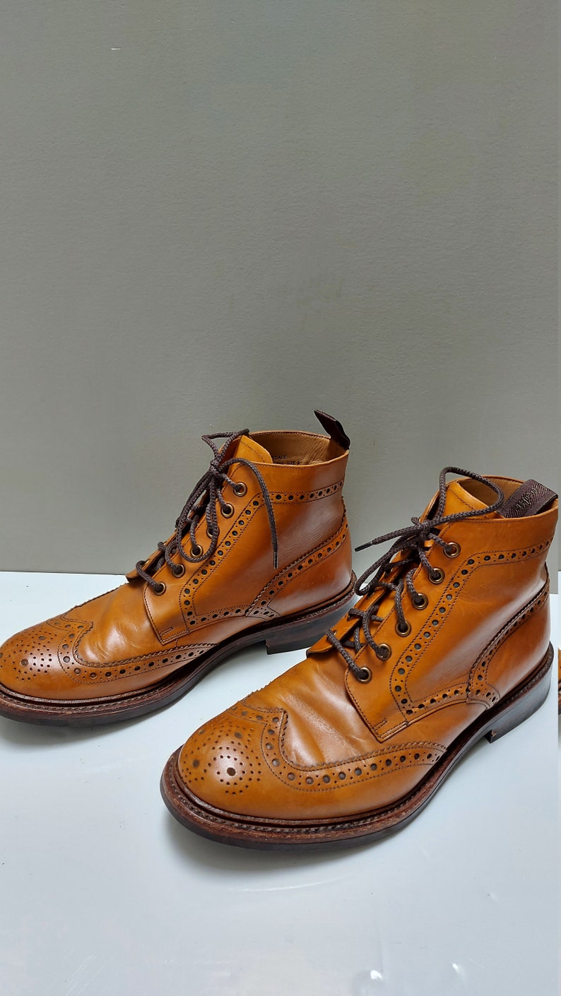 May include: A pair of brown leather brogue boots with a lace-up closure. The boots have a wingtip design and a decorative pattern of small holes.