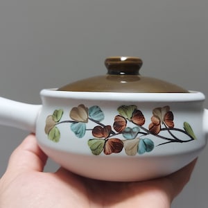 Può includere: Piatto da forno in ceramica bianca con coperchio marrone e un motivo floreale con foglie verdi, blu e marroni.