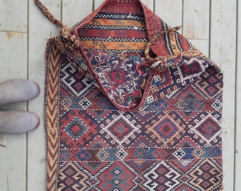 May include: A traditional woven rug with a geometric pattern in shades of red, blue, and yellow. The rug is folded in half and has a fringed edge.