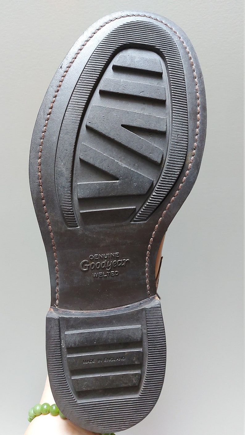 May include: Close-up of the brown leather sole of a shoe with a Goodyear Welted label and the text "Made in England".