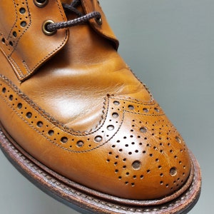 May include: Close-up of a brown leather brogue boot with a wingtip design and decorative perforations.