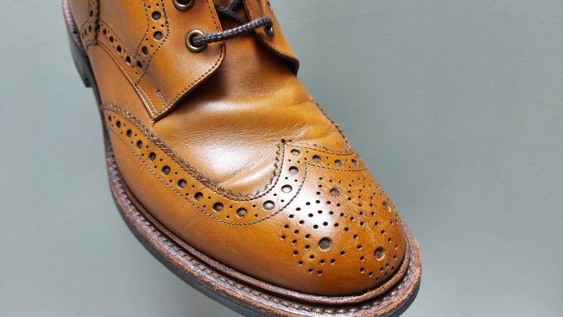 May include: Close-up of a brown leather brogue boot with a wingtip design and decorative perforations.