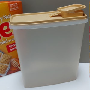 May include: A clear plastic container with a beige lid and a beige spout. The container is designed for storing dry goods, such as cereal or pasta. The lid has a handle for easy opening and closing.