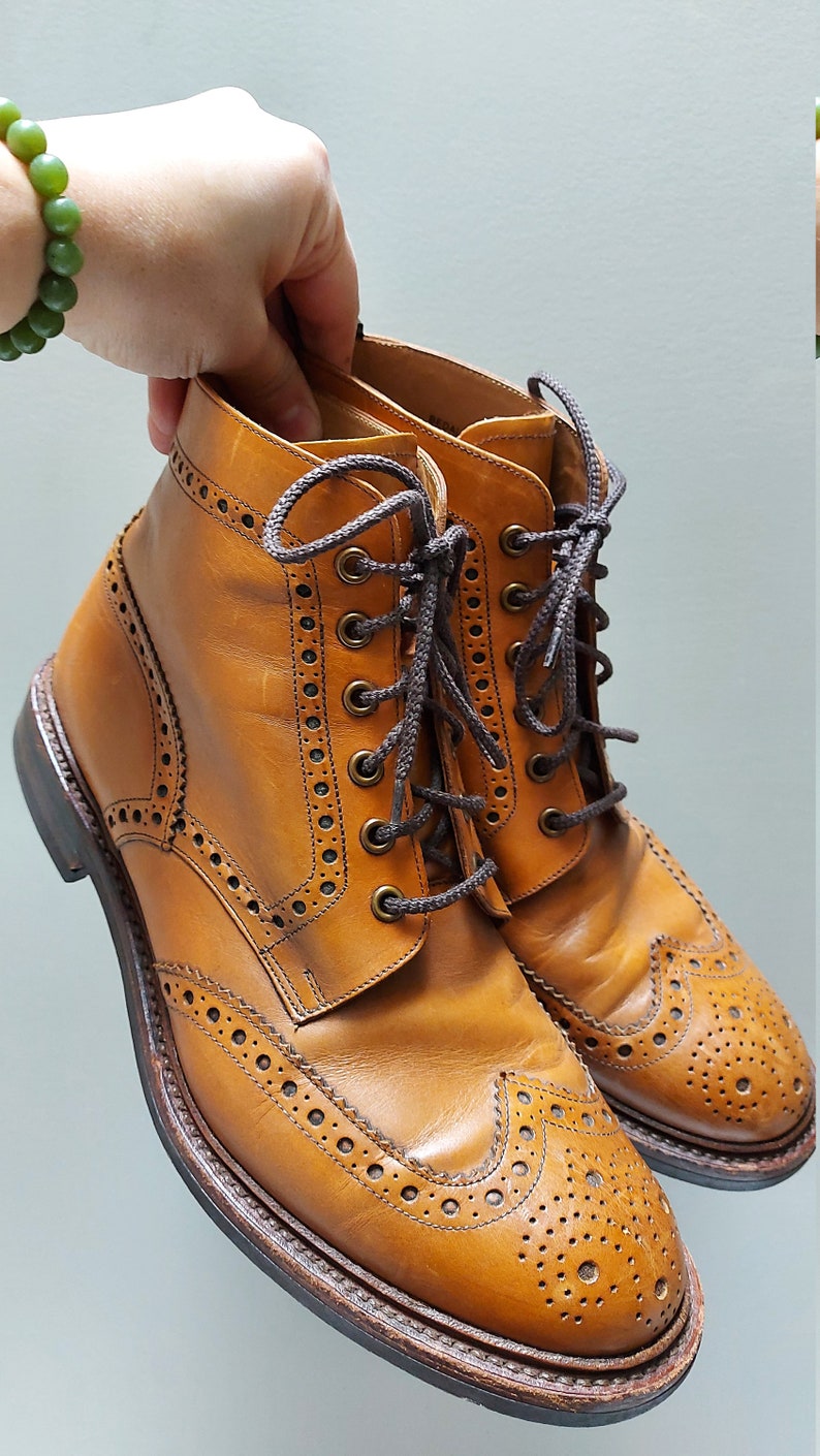 May include: A pair of brown leather brogue boots with a lace-up closure. The boots have a wingtip design and a textured sole.