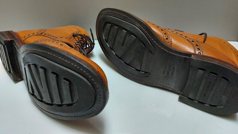 May include: A pair of brown leather brogue boots with a black rubber sole. The sole has the text "Genuine Goodyear Welt" printed on it.