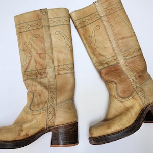 Puede incluir: Un par de botas vintage hasta la rodilla en color beige claro. Las botas presentan costuras decorativas y una puntera cuadrada. Tienen un tacón grueso y suela de plataforma, lo que les da un estilo retro. Miden unos 30 cm de alto.