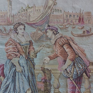 Peut inclure: Une tapisserie représentant une scène à Venise avec deux personnages en costumes d'époque debout sur un balcon surplombant un canal. Les personnages sont vêtus de vêtements colorés et interagissent l'un avec l'autre. L'arrière-plan présente une ville avec des bâtiments et des bateaux.