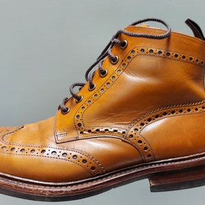 May include: A pair of brown leather brogue boots with a lace-up closure. The boots have a wingtip design and a textured sole.