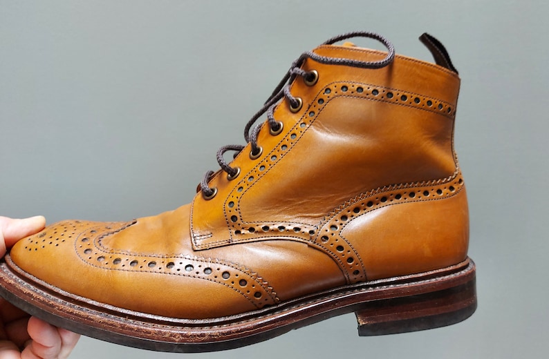 May include: A pair of brown leather brogue boots with a lace-up closure. The boots have a wingtip design and a textured sole.