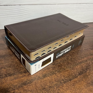 May include: A white ceramic mug with a black handle and the text "But First, Coffee" in a handwritten style. The mug is on a white surface. The mug is approximately 4 inches tall.