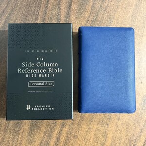 May include: A blue leather-bound Bible next to its black box. The box has the text "NIV Side-Column Reference Bible" and "Personal Size". The Bible is from the Premier Collection.