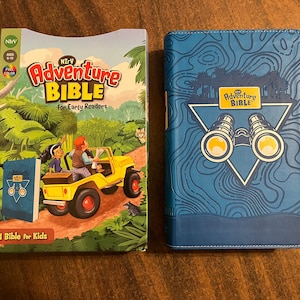 May include: Two blue and yellow Adventure Bible books. The smaller book is for early readers and features a cartoon illustration of a jeep driving through a jungle. The larger book has a blue cover with a triangle and binoculars design.
