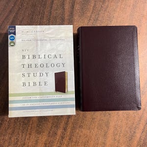May include: Two Bibles are displayed. One is a hardback with a burgundy cover. The other is a paperback with the title "NIV Biblical Theology Study Bible" and the author's name, D. A. Carson, printed on the cover.