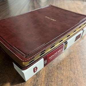 May include: A brown leather-bound Holy Bible with gold accents and the text "THINLINE BIBLE RED LETTER EDITION" on the spine. The bible is sitting on a white box with the text "PRINT" and "ZONDERVAN" on it.
