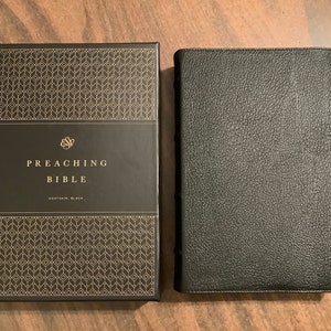 May include: A black leather-bound book with the title "Preaching Bible" on the cover. The book is in a black box with a gold geometric pattern.