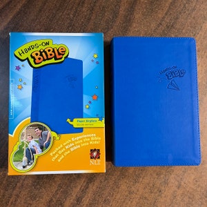 May include: A blue hardcover book with the title "Hands-on Bible" and a paper airplane graphic. The book is part of a set that includes activities to help kids learn about the Bible.