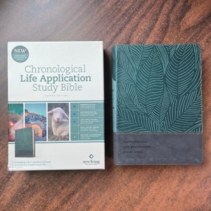 May include: A green and gray hardcover study Bible with the title "Chronological Life Application Study Bible - Second Edition -" on the front cover. The cover features a leafy pattern and the New Living Translation logo.