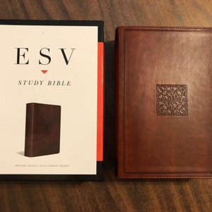 May include: A brown leather-bound ESV Study Bible with a Celtic knot design on the cover. The Bible is closed and sitting on a wooden surface.