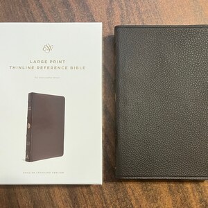May include: A brown leather Bible next to its white box. The box reads "LARGE PRINT THINLINE REFERENCE BIBLE" and "English Standard Version". The Bible has a dark brown cover with a textured surface.