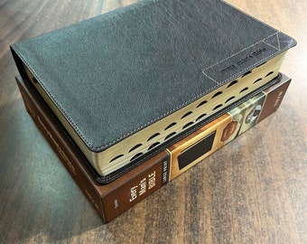 Op de afbeelding: Een zwarte lederen gebonden Bijbel met goudkleurige randen en de tekst "Every Man's Bible" op de rug. De Bijbel is gesloten en ligt op een bruine doos met de tekst "Every Man's Bible" en "Large Print" op de zijkant.