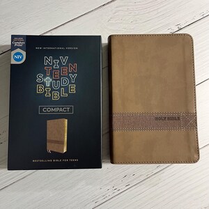 May include: A brown leather-bound NIV Teen Study Bible with the words "HOLY BIBLE" embossed on the front cover. The Bible is closed and the spine is visible. The Bible is a compact size.