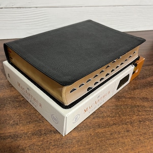 May include: A black leather-bound Bible with gold-toned edges and the text "The MacArthur Study Bible" printed on the cover.