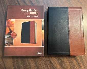 Op de afbeelding: Een zwarte en bruine leren gebonden Bijbel met de titel "Every Man's Bible" en "Large Print" op de kaft. De Bijbel zit in een doos met een afbeelding van een man die op een pad in de woestijn loopt.