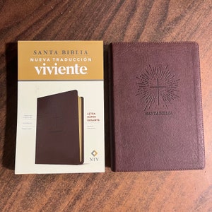 May include: A brown leather-bound Bible with the title "SANTA BIBLIA NUEVA TRADUCCIÓN viviente" on the cover. The Bible has a gold cross design and the words "SANTA BIBLIA" embossed on the front cover.
