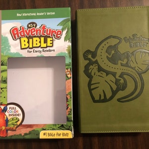 May include: A green hardcover book with the title "The Adventure Bible" for early readers. The cover features a green lizard with a black outline on a green leaf background.