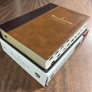 May include: A brown leather-bound Bible with gold lettering that reads "The MacArthur Study Bible, NKJV".