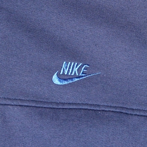 May include: Close-up of a navy blue Nike jacket. The Nike logo is embroidered in light blue on the upper left chest. The jacket has a full zipper and a contrasting light blue panel on the right side.