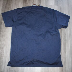 Pu&ograve; includere: Una polo a maniche corte blu navy con colletto a righe gialle e bianche.