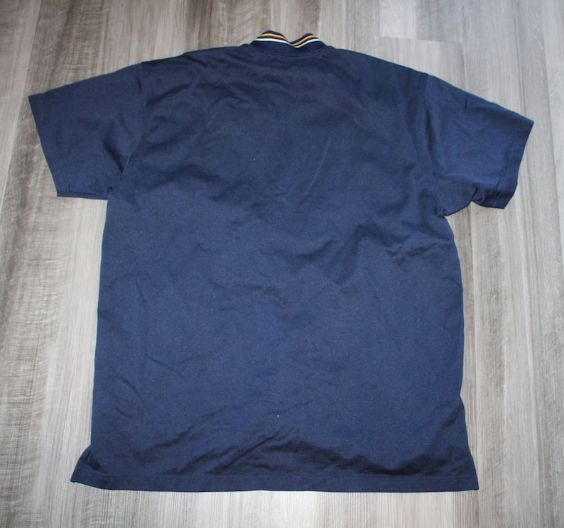 Pu&ograve; includere: Una polo a maniche corte blu navy con colletto a righe gialle e bianche.