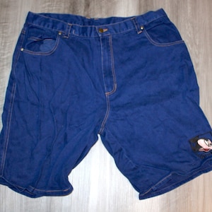 May include: Blue denim shorts with a Mickey Mouse patch on the right leg. The patch is black and white with the words "Disney World" printed on it.