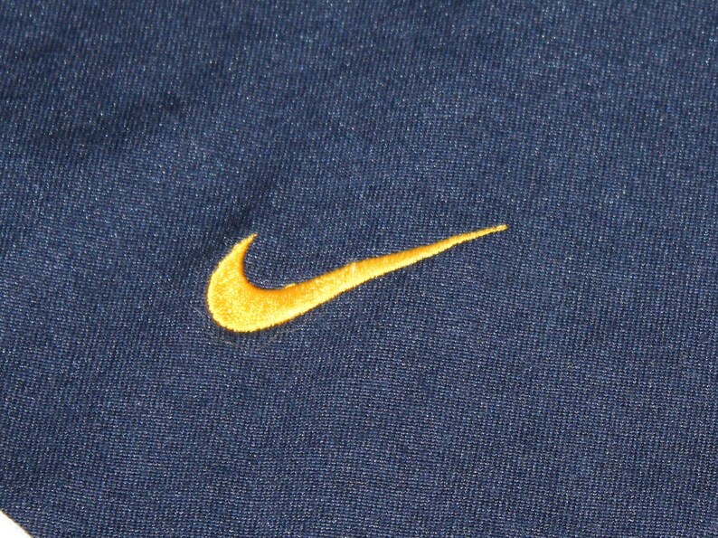 Pu&ograve; includere: Un tessuto blu navy con un logo Nike swoosh ricamato in oro.