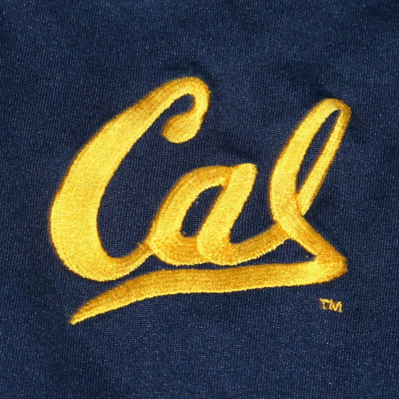 Pu&ograve; includere: Un toppa in tessuto blu navy con la parola "Cal" ricamata in filo giallo. La parola &egrave; stilizzata con un carattere corsivo e un simbolo di marchio registrato si trova sotto la parola.