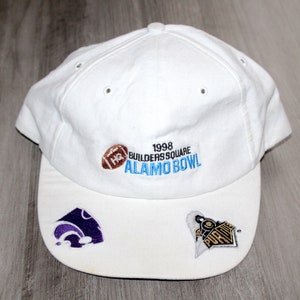 Op de afbeelding: Witte baseballpet met een gebogen klep. De pet heeft geborduurde tekst en logo's voor de 1998 Builders Square Alamo Bowl, een voetbal en twee teamlogo's. De pet is gemaakt van een zachte stof.